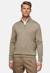 Pullover beige a mezza zip realizzato in tessuto testurizzato, con maniche lunghe e polsini a coste. Indossato sopra una camicia bianca con colletto.