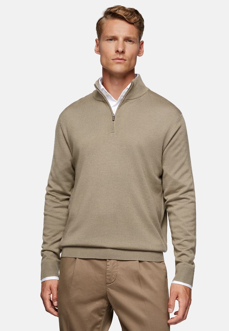 Pullover beige a mezza zip realizzato in tessuto testurizzato, con maniche lunghe e polsini a coste. Indossato sopra una camicia bianca con colletto.