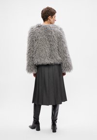 Futrzana szara kurtka, plisowana ciemnoszara spódnica, czarne buty do kolan. Teksturowane wykończenie kurtki, gładki materiał spódnicy i butów.