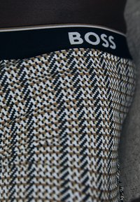 Herrenboxershorts mit einem Hahnentrittmuster in Schwarz, Weiß und Braun. Schwarzer elastischer Bund mit "BOSS"-Logo in Weiß. Weiche Stoffstruktur.