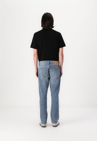 Svart kortermet t-skjorte og lyseblå jeans med lærpatch bak, med klassisk femlommestil og en avslappet passform.
