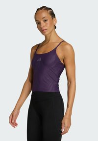 Purple sports tank top with thin straps, featuring a textured design and a small logo, paired with black high-waisted leggings.