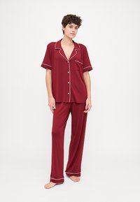 Burgundy pajama set with short button-up top featuring white piping and pocket, paired with loose-fitting pants. Smooth fabric texture.