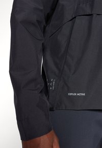 Schwarze wasserdichte Jacke mit glatter Textur, verstellbaren Manschetten und CEPLX ACTIVE-Branding am Saum. Minimalistisches Design.
