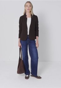 Hnědý blazer, bílá košile, modré džíny a hnědé tenisky. Model drží hnědou tašku. Pozadí je jednoduché a bílé.