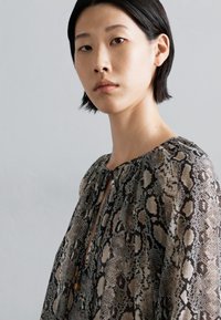 Vloeiende blouse met een slangenprint in beige en bruine tinten. Sleutelgat halsontwerp met een lichte textuur en zachte draping.