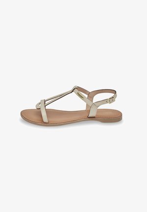 Flat sandals made of light beige leather, featuring a minimalist design with crossed straps and a buckled ankle strap. Smooth texture, open toe.