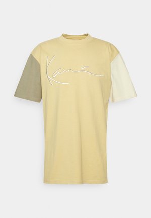 Short-sleeve t-shirt in muted yellow, featuring a white embroidered logo. Color-blocked sleeves in light green and pale cream. Cotton material.