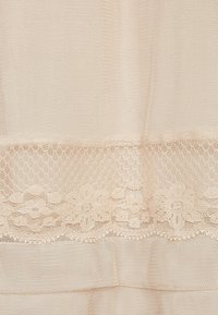 Beige spets tyg med ett blommönster, som har ett texturerat nätöverdrag och en slät, delikat spetskant nedtill.