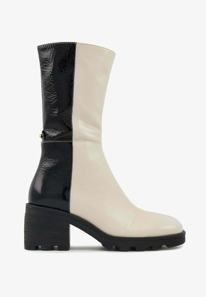 Botte à genoux bicolore en cuir brillant noir et crème, dotée d'un talon carré et d'une semelle en caoutchouc texturé pour une meilleure adhérence.