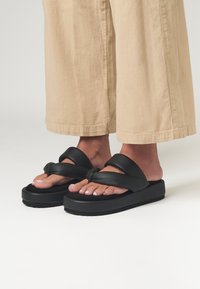 Sandali platform neri con design a fascia larga, realizzati in materiale morbido simile alla gomma. Presentano una suola texturizzata per aderenza e comfort.