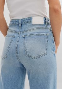 Jean en denim bleu clair à coupe droite, doté d'une étiquette blanche unie à la taille et de deux poches arrière avec un design classique de coutures.