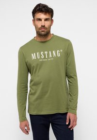 Långärmad olivgrön t-shirt i bomull med rund halsringning. Har vit text "MUSTANG JEANS COMPANY SINCE 1932" på framsidan.