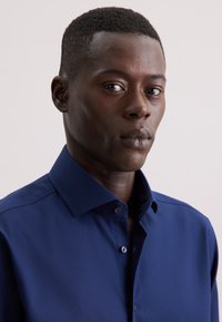 Marineblauwe button-up shirt van een gestructureerde stof, met een spread collar en subtiele knopen, tentoongesteld tegen een neutrale achtergrond.