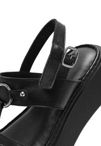 Sandalo in pelle nera con una fascia ampia, fibbia regolabile, dettaglio circolare e suola spessa con finitura texture.