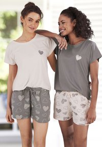 Divas modeļi valkā īsām piedurknēm tops ar sirds rakstiem un atbilstošiem šortiem. Viens tops ir gaiši bēšs, otrs - tumši pelēks; šorti ir ar sirds motīviem.