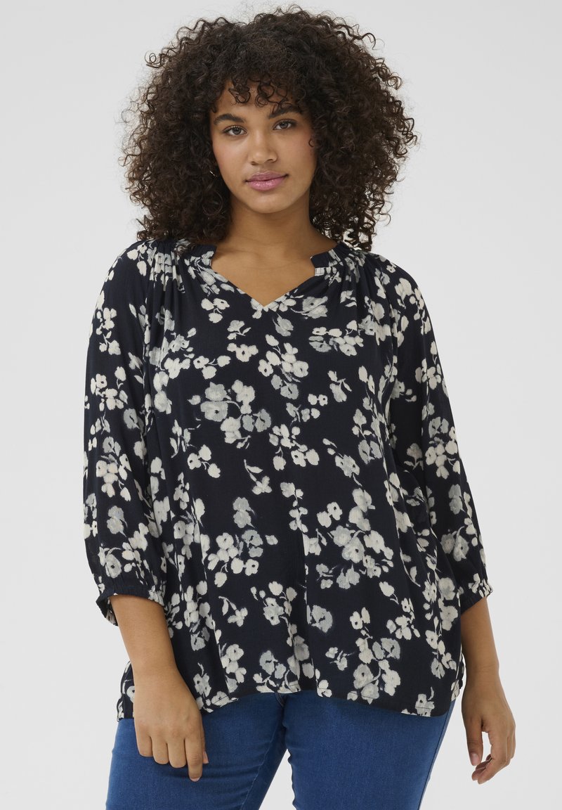 Blouse florale bleu marine avec de légers motifs de fleurs blanches, décolleté en V, manches trois-quarts et tissu doux. Associée à un jean bleu.