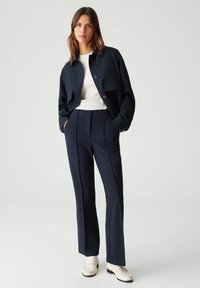 Marineblauwe cropped jas met knopen en zak, gecombineerd met slim-fit marineblauwe broek en crèmekleurige loafers. Zachte stof en op maat gemaakte design.