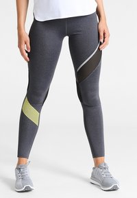 Szare legginsy sportowe z czarnymi wstawkami z siateczki i żółtymi akcentami. Dopasowany krój o fakturowanej powierzchni, w połączeniu z szarymi trampkami.