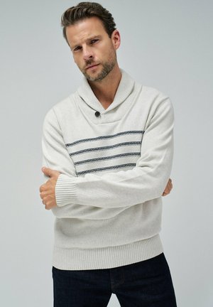 Jersey gris claro con cuello chal, con rayas horizontales en blanco y negro en el pecho. Puños y dobladillo acanalados.