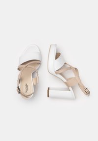 Sandalias de tacón alto en blanco y beige con tiras, tacón grueso, material de cuero suave y hebilla en el tobillo para ajuste.