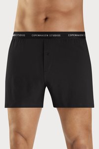 Sorte boksershorts laget av glatt stoff med knappelukking. Midjeelasten har hvit tekst som leser "COPENHAGEN STUDIOS."