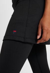 Svart träningskläder med en figursydd linne och leggings. Mærkbar röd och blå logotypdetalj på sidan, mjuk textur och elegant design.