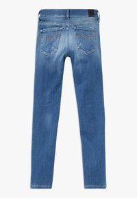 Jeans de mezclilla azul, de corte ajustado, con dos bolsillos traseros con costuras claras, textura desgastada y una etiqueta de cuero en la cinturilla.