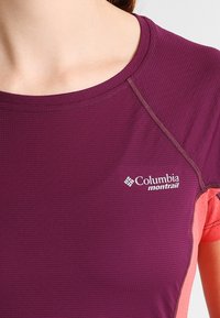 Lila träningströja med texturerat tyg, som har korta ärmar och en rosa detalj på sidan. Inkluderar Columbia Montrail-logotypen.