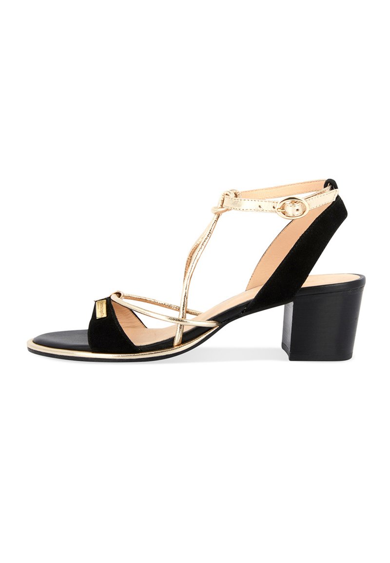 Sandale à talon haut en daim noir avec des accents métalliques dorés, bout ouvert, design en T, boucle à la cheville et talon épais noir.