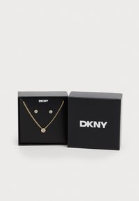 Gold-tone jewelry set featuring a necklace with a round pendant and matching stud earrings, displayed in a black DKNY box.