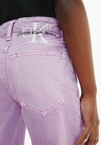 Jeans in denim lilla con due tasche posteriori, un logo Calvin Klein Jeans sulla vita e dettagli di cucitura a contrasto.