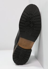 Musta nahkakenkien pohja, jossa on karhea kuvio. Sisältää tekstuuripintaisen mustan kumipohjan ja kontrastoivan puuosan.