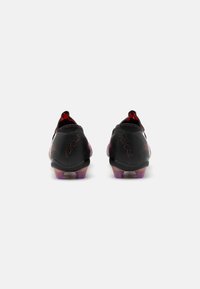 Foulées de football noires avec un dessus texturé, accents rouges et semelles transparentes teintées de violet. Présente un design épuré pour la performance.