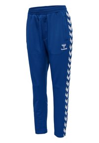 Pantalon de sport bleu avec des bandes chevrons blanches sur les côtés et logo Hummel sur la cuisse supérieure, avec une ceinture élastique et des poches.