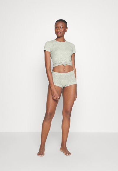 Svetlošedé skrátené tričko s uzlom vpredu, kombinované s prispôsobenými vysokými šortkami, obidve vyrobené z jemného, elastického materiálu.