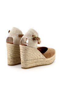 Sandali con zeppa in suede marrone, dettagli in tessuto intrecciato e cinturino alla caviglia. Il tacco avvolto in corda aggiunge texture; design con apertura sul retro e punta arrotondata.