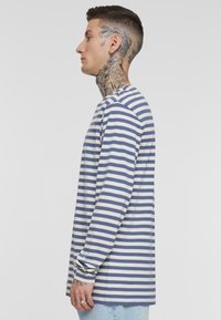 Langermet t-skjorte i marineblå og kremfargede striper, laget av myk bomull, med rund hals og avslappet passform, vist på en modell fra siden.