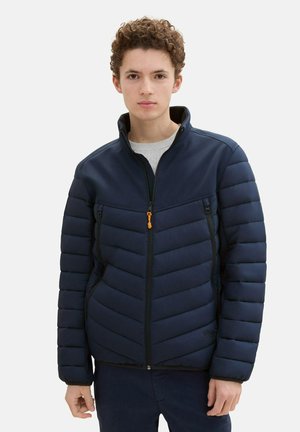 Marineblaue Steppjacke mit Reißverschluss vorne, hohem Kragen und Zickzack-Steppmuster. Enthält zwei Reißverschlusstaschen und einen orangen Reißverschlusszug.