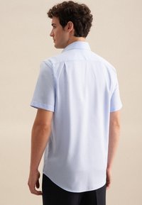 Camicia azzurra a maniche corte con colletto classico, tessuto liscio e orlo curvo. Presenta maniche arrotolate e un design pulito e minimalista.