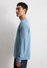 Maglione a maniche lunghe di colore azzurro chiaro in tessuto morbido, con scollatura a girocollo e polsini a coste, dalla vestibilità rilassata e con una texture sottile.