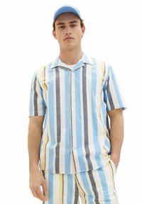 Kurzärmliges, knöpfbares Hemd in hellblau, weiß, gelb und grau mit vertikalen Streifen; kombiniert mit passenden gestreiften Hosen. Aus Baumwollmaterial.