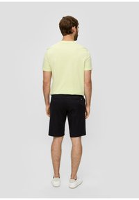 Light green short-sleeve t-shirt, plain design, paired with black shorts. Model wearing white sneakers, shown from the back.