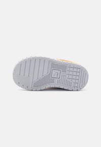 Suela de zapatilla de caucho blanco con una superficie texturizada, que presenta ranuras y patrones. Acentos naranjas y rosas cerca del talón.