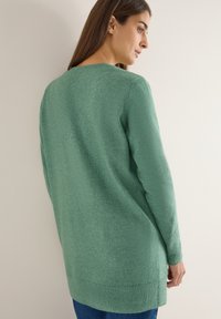 Zelený pletený svetr s dlouhými rukávy a žebrovaným lemem. Má kulatý výstřih a texturovaný vzor, navržený pro uvolněný střih.