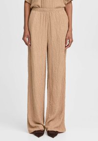 Beige weit geschnittene Hose aus einem strukturierten, zerknitterten Stoff. Elastischer Bund, gefaltete Details und fließendes Design, das bis zum Boden reicht.