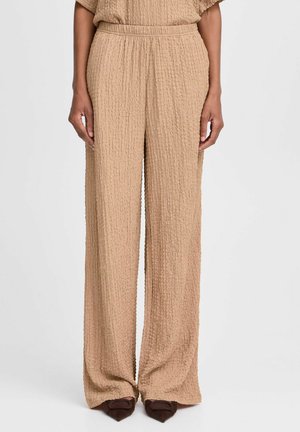 Beige weit geschnittene Hose aus einem strukturierten, zerknitterten Stoff. Elastischer Bund, gefaltete Details und fließendes Design, das bis zum Boden reicht.