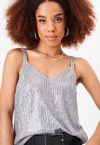 Silver sequin tank top with a V-neck, thin straps, and a loose fit. Features vertical sequin patterns and is paired with a black belt.