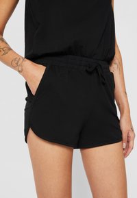 Sorte atletiske shorts lavet af blød stof, med en elastisk talje, snor og sidelommer samt en let slidse i nederste kant.