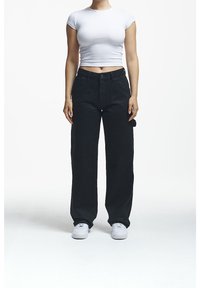Pantaloni neri a gamba larga con una texture liscia, vita alta e tasche laterali, abbinati a un crop top bianco aderente e sneaker bianche.